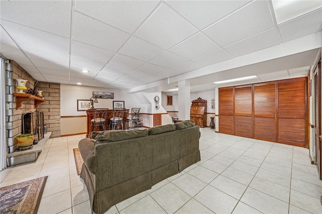 living room featuring a dry bar, light tile patterned flooring, a drop ceiling, and a large fireplace