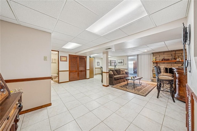 living area featuring light tile patterned floors, a drop ceiling, baseboards, and a fireplace