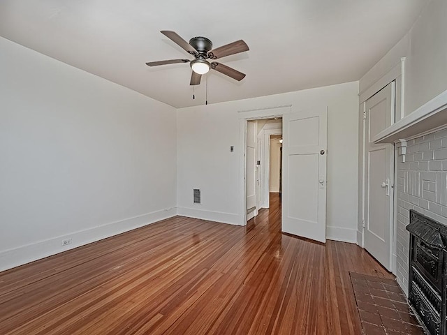 unfurnished living room featuring wood finished floors, visible vents, baseboards, a fireplace, and ceiling fan