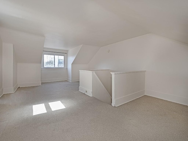 additional living space featuring vaulted ceiling, light colored carpet, and baseboards