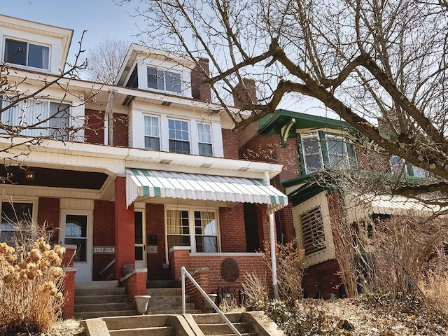 american foursquare style home featuring covered porch, brick siding, and a chimney