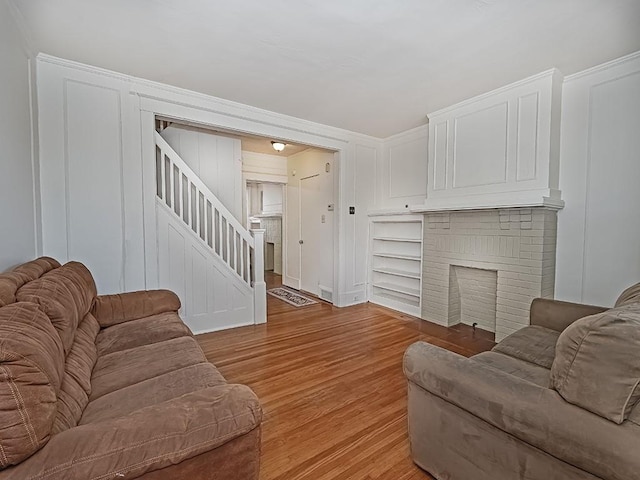 living area with light wood-style floors, a brick fireplace, stairs, and a decorative wall