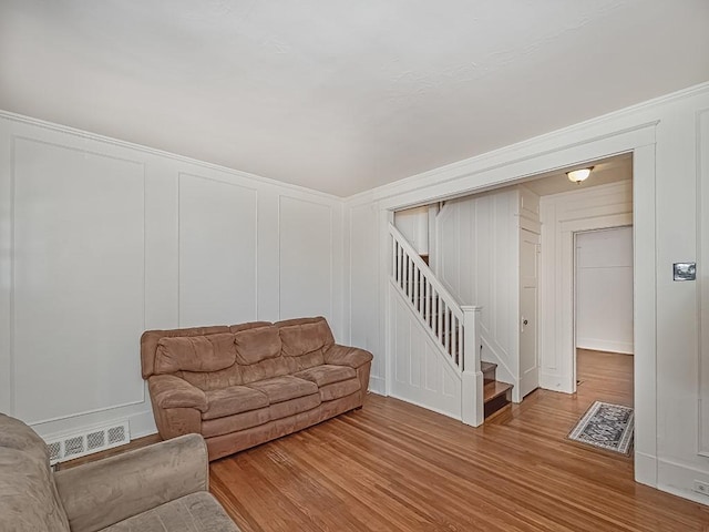 living area featuring stairway, a decorative wall, wood finished floors, and visible vents