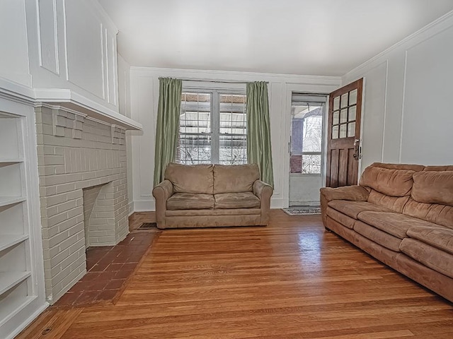 living area with a brick fireplace, wood finished floors, crown molding, and a decorative wall