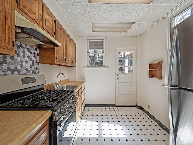 kitchen featuring brown cabinetry, baseboards, a sink, under cabinet range hood, and appliances with stainless steel finishes