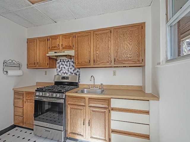 kitchen featuring under cabinet range hood, stainless steel gas range, light countertops, and a sink