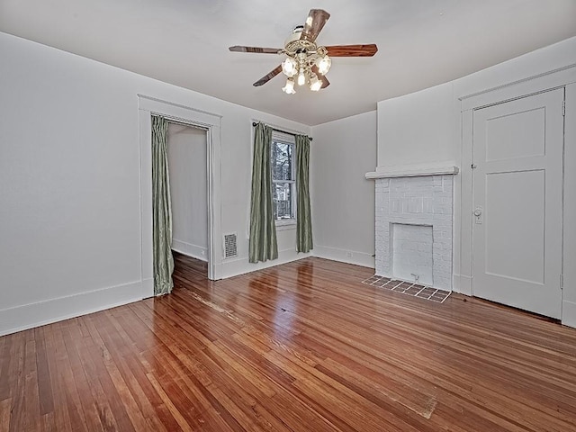 unfurnished living room featuring hardwood / wood-style floors, a ceiling fan, baseboards, visible vents, and a fireplace