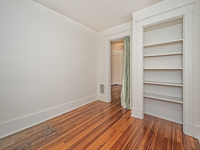 unfurnished bedroom with wood finished floors, visible vents, a closet, and baseboards