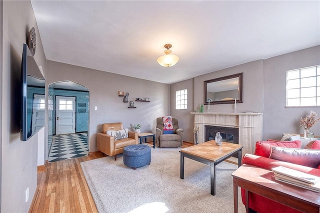 living room featuring a glass covered fireplace, arched walkways, and light wood-style flooring