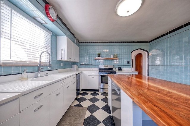 kitchen with a sink, wood counters, white cabinetry, stainless steel appliances, and light floors