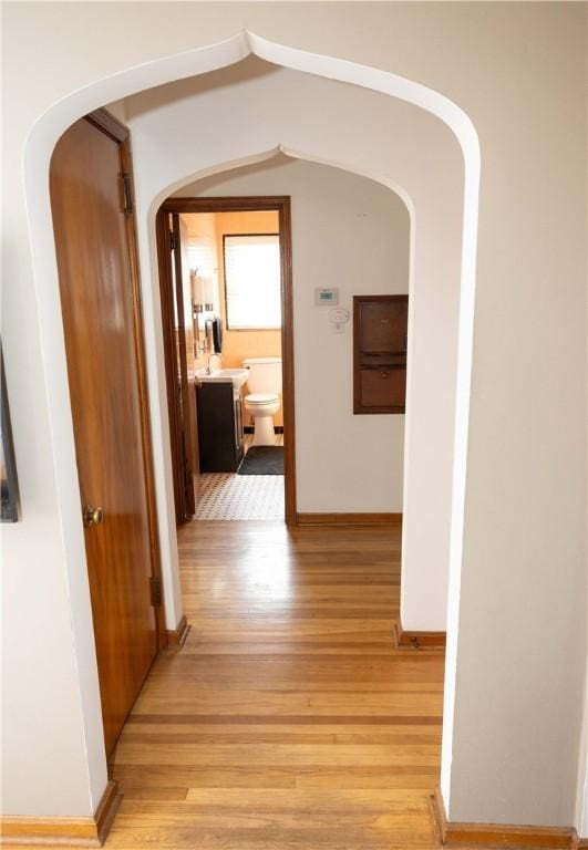 corridor featuring baseboards, arched walkways, and light wood-style floors