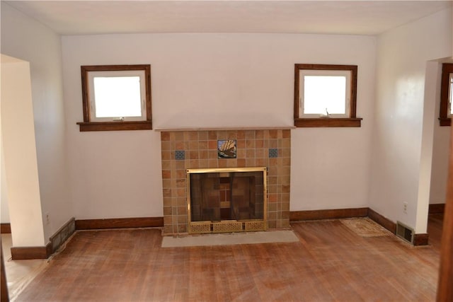 unfurnished living room featuring a healthy amount of sunlight, wood finished floors, and a tile fireplace