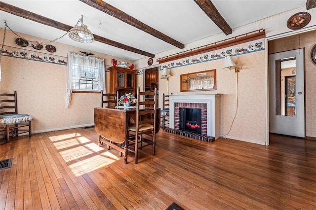 dining room featuring visible vents, a brick fireplace, baseboards, hardwood / wood-style floors, and beam ceiling