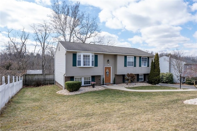 split foyer home featuring brick siding, a front yard, and fence