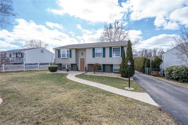 bi-level home featuring brick siding, aphalt driveway, fence, and a front lawn