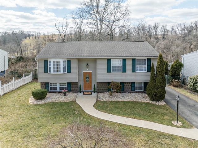 split foyer home featuring aphalt driveway, brick siding, a front yard, and fence