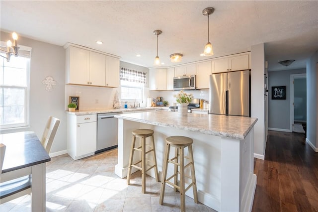 kitchen featuring hanging light fixtures, white cabinets, appliances with stainless steel finishes, and a kitchen island