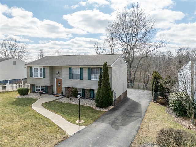 split foyer home featuring aphalt driveway, brick siding, a front yard, and fence