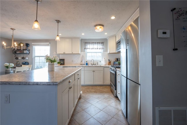 kitchen featuring visible vents, a kitchen island, stainless steel appliances, white cabinets, and backsplash