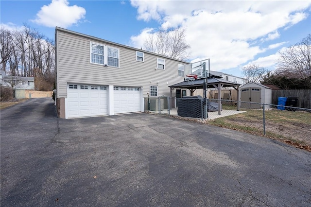 view of front of property featuring fence, a gazebo, a garage, driveway, and a storage unit