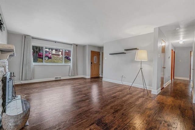 unfurnished living room with visible vents, wood finished floors, baseboards, and a fireplace with raised hearth