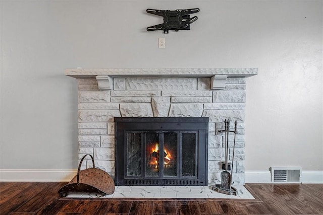 details with a stone fireplace, wood finished floors, visible vents, and baseboards