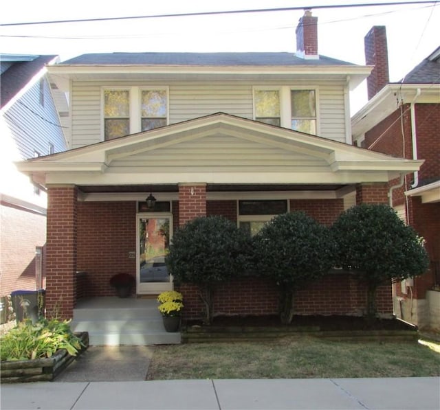 view of front of home with covered porch, brick siding, and a chimney