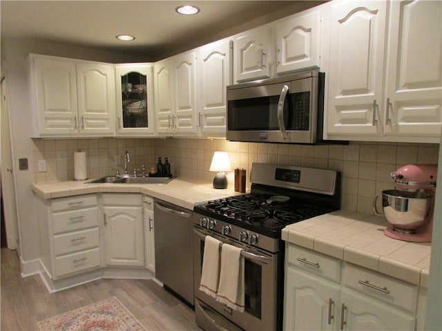 kitchen with a sink, stainless steel appliances, tile counters, and white cabinets