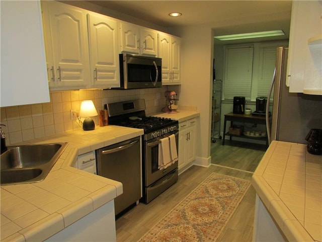 kitchen featuring tile countertops, appliances with stainless steel finishes, white cabinetry, and wood finished floors