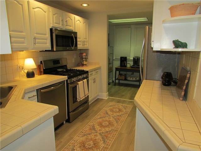 kitchen with tile countertops, appliances with stainless steel finishes, wood finished floors, white cabinetry, and open shelves