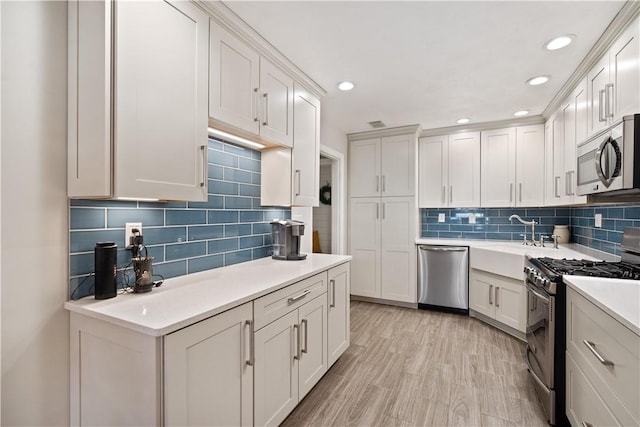 kitchen with tasteful backsplash, light countertops, appliances with stainless steel finishes, white cabinets, and a sink