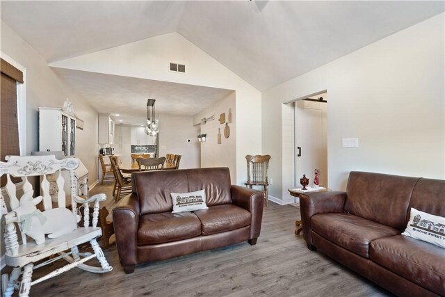 living area with visible vents, baseboards, wood finished floors, and vaulted ceiling