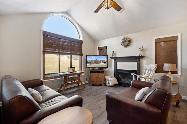 living room with a tiled fireplace, baseboards, ceiling fan, and wood finished floors