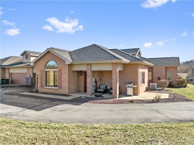 view of front of home with central AC unit, brick siding, roof with shingles, and a patio area