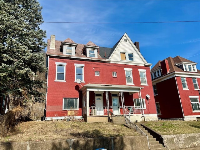 view of front facade with brick siding, covered porch, and a chimney