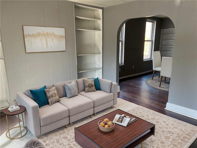 living room featuring arched walkways, built in shelves, baseboards, and wood finished floors