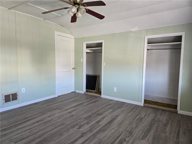 unfurnished bedroom featuring baseboards, visible vents, ceiling fan, dark wood-type flooring, and multiple closets