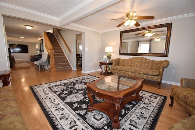 living area featuring stairway, baseboards, wood finished floors, and crown molding