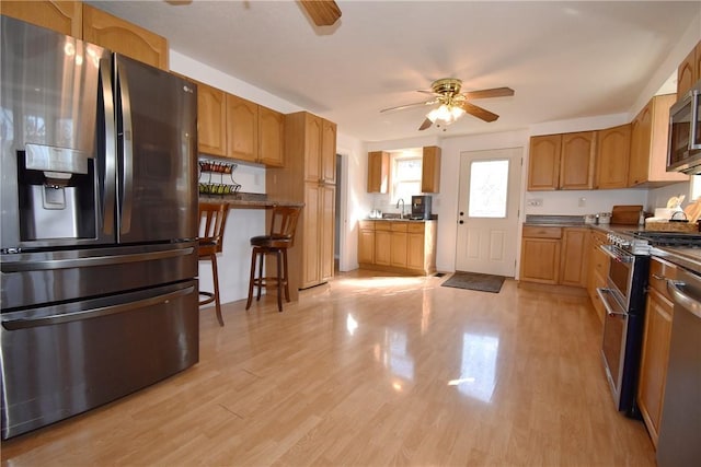 kitchen with dark countertops, ceiling fan, a kitchen bar, light wood-type flooring, and stainless steel appliances