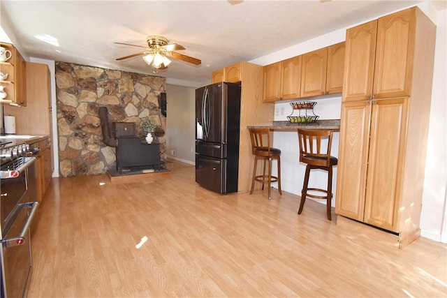 kitchen featuring stainless steel appliances, a breakfast bar area, a ceiling fan, and light wood finished floors