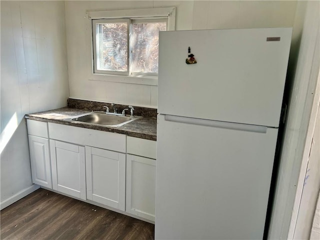 kitchen featuring freestanding refrigerator, a sink, dark wood-type flooring, white cabinetry, and dark countertops