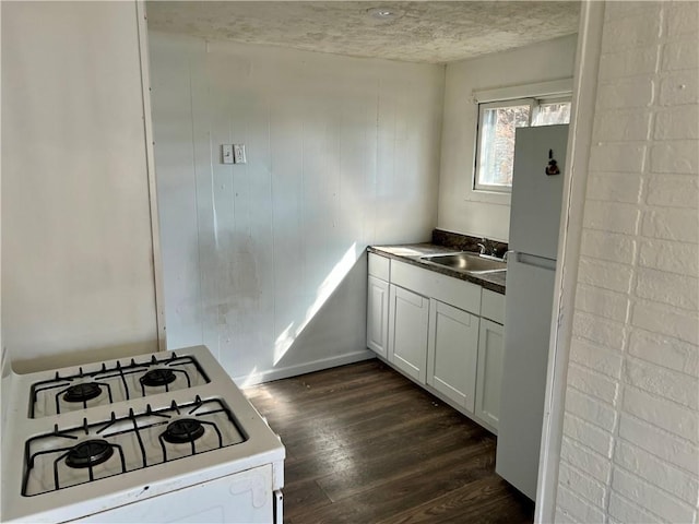 kitchen with a sink, white appliances, dark wood-type flooring, and white cabinets