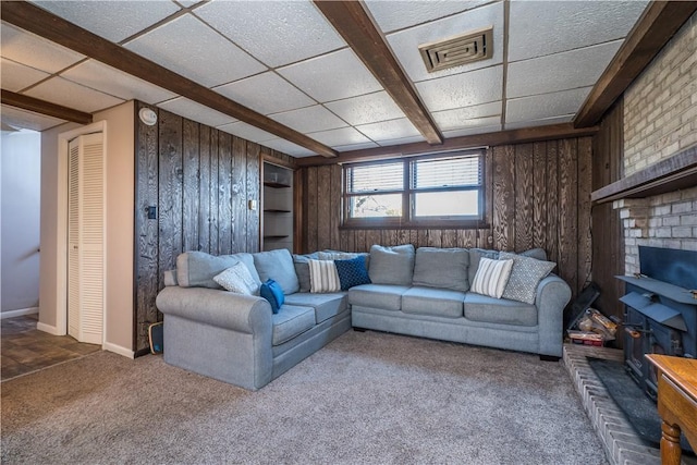 living area featuring a drop ceiling, visible vents, wooden walls, and carpet flooring