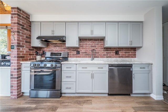 kitchen featuring under cabinet range hood, gray cabinets, appliances with stainless steel finishes, light wood-style floors, and a sink