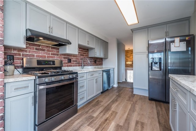 kitchen with gray cabinets, under cabinet range hood, a sink, tasteful backsplash, and appliances with stainless steel finishes