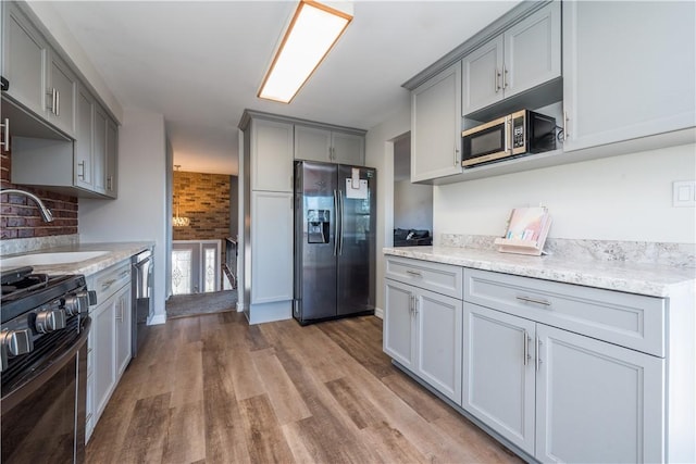 kitchen with light stone counters, gray cabinets, a sink, appliances with stainless steel finishes, and light wood-type flooring