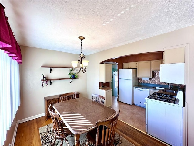 dining space with an inviting chandelier, wood finished floors, arched walkways, and a textured ceiling