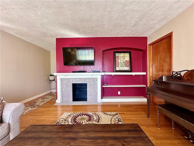 living room with a fireplace, wood finished floors, baseboards, and a textured ceiling