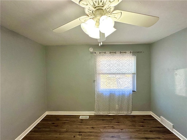 spare room featuring dark wood-style floors, visible vents, a ceiling fan, and baseboards