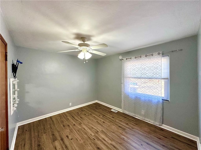 spare room with dark wood-style floors, visible vents, a ceiling fan, and baseboards